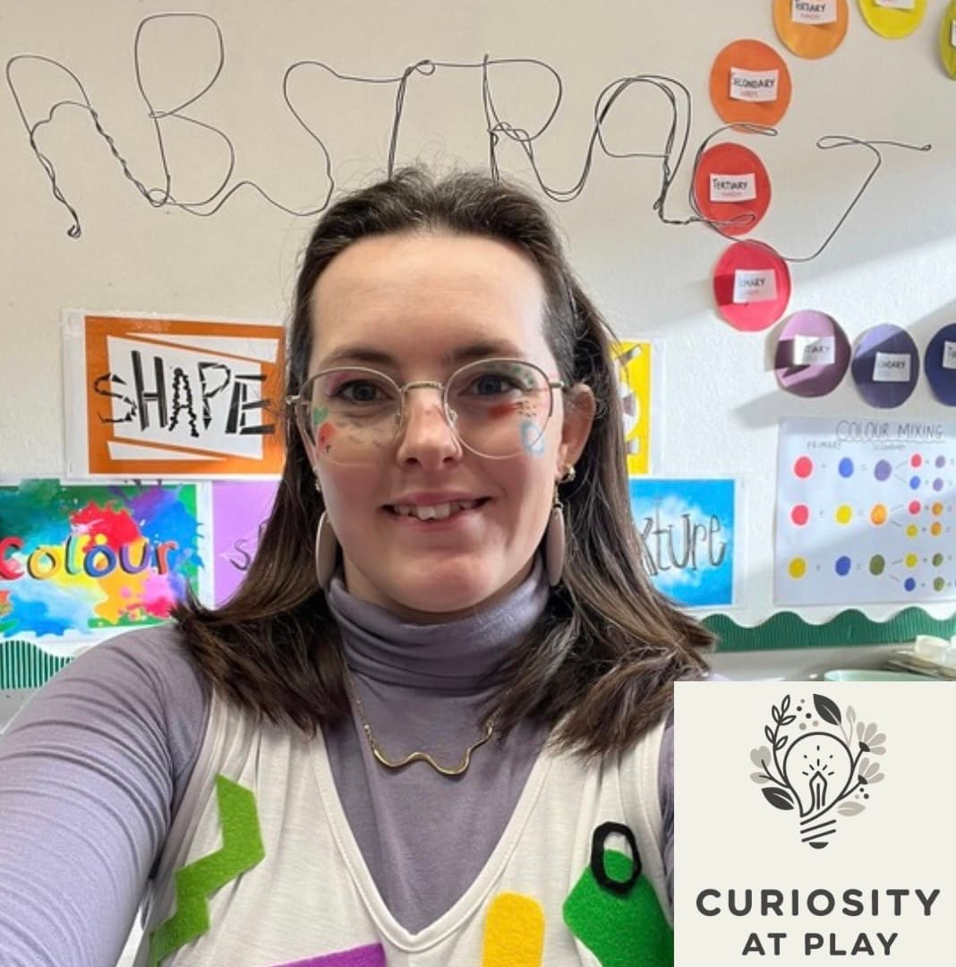 Smiling woman with face paint in an art classroom with a Curiosity at Play logo.