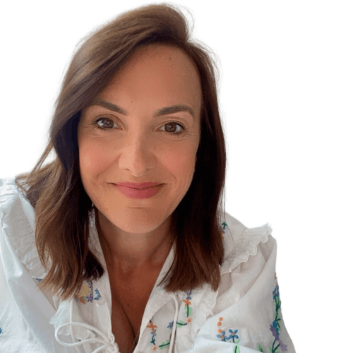 Smiling woman with shoulder-length brown hair wearing a white blouse with colorful floral embroidery.