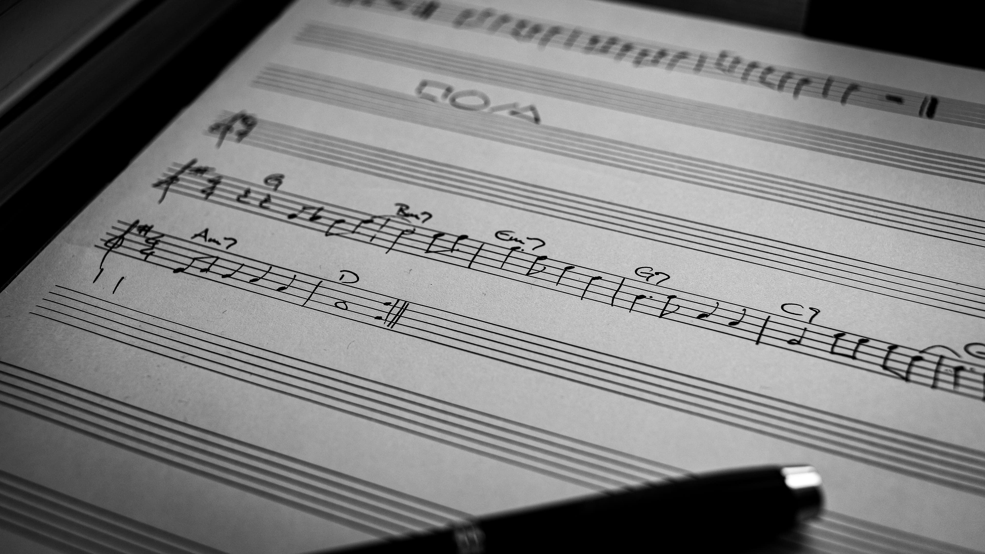 Handwritten musical notes and chord symbols on staff paper with a pen in the foreground.