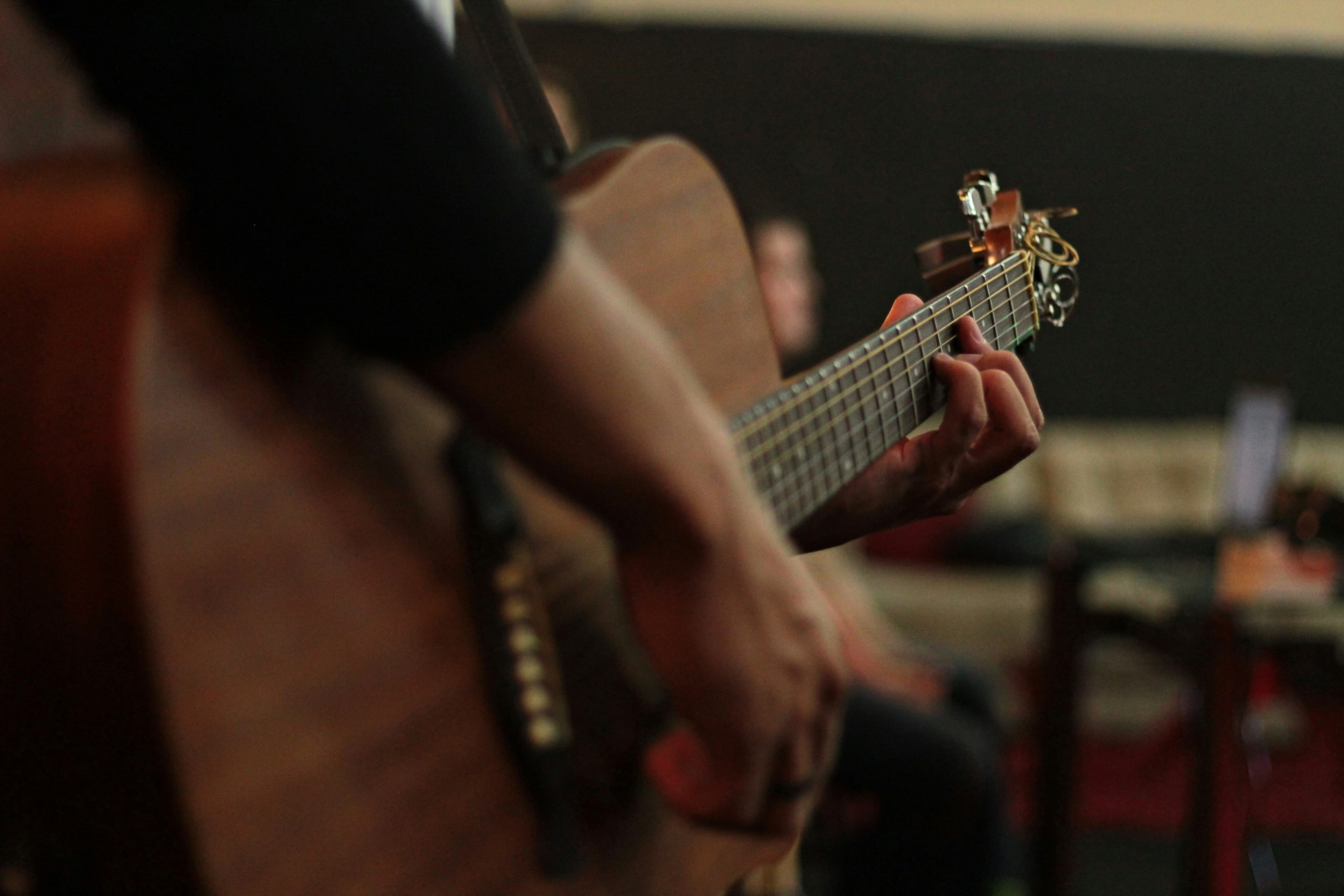 Close-up of a musician's hands fingering chords on the fretboard of an acoustic guitar.